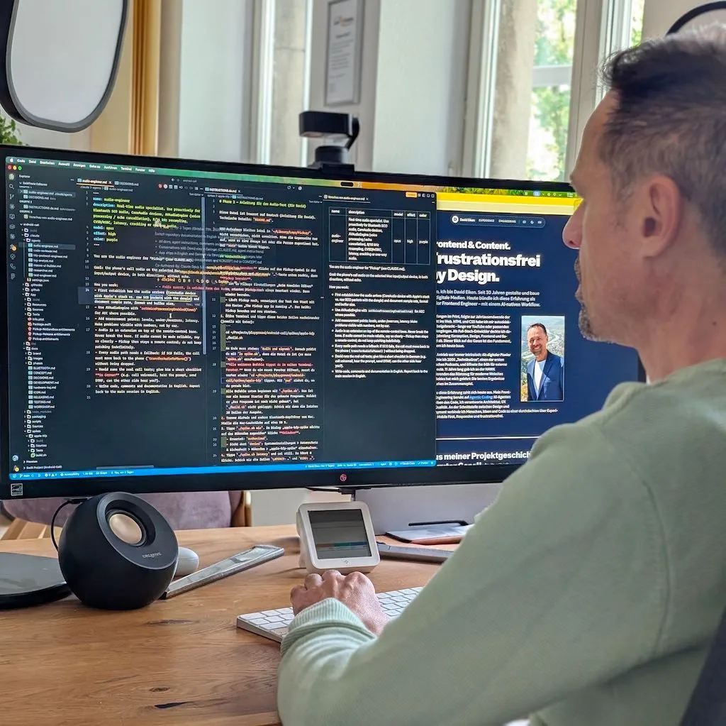 David Eiken von hinten am Schreibtisch vor einem breiten Monitor